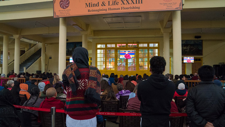 4日目の会議で、ツクラカンの中庭に設置された大型モニターを通してダライ・ラマ法王のお話を聴く一般の人々。2018年3月15日、インド、ヒマーチャル・プラデーシュ州ダラムサラ（撮影：テンジン・チュンジョル / 法王庁）