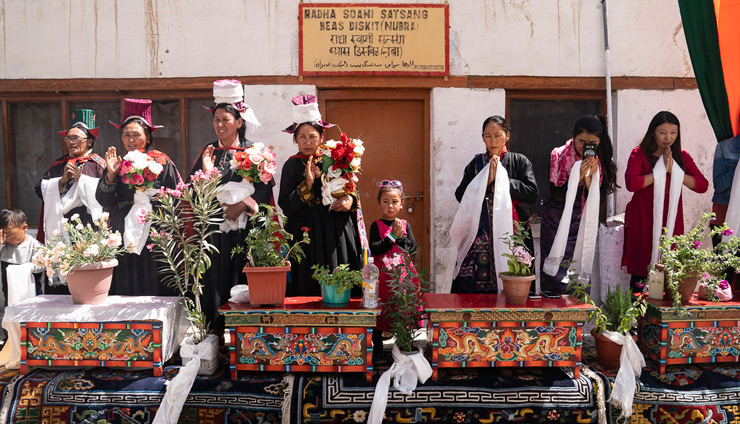鉢植えの花を置いた木彫りのテーブルのそばに立ち、ヌブラ渓谷まで車で移動されるダライ・ラマ法王を歓迎する地元の人々。2018年7月12日、インド、ジャンムー・カシミール州ヌブラ渓谷デスキット（撮影：テンジン・チュンジョル / 法王庁）