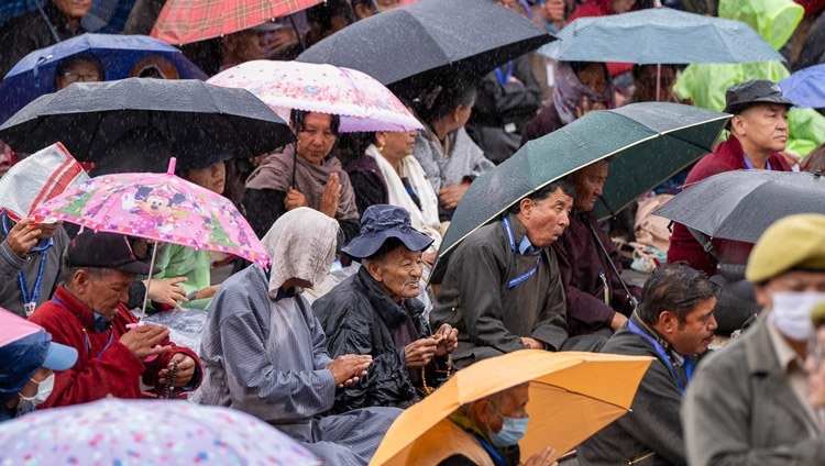 ダライ・ラマ法王が観音菩薩の灌頂を授けられる際、傘をさして雨をよけながらも、法王の話に耳を傾ける聴衆たち。2023年7月23日、インド、ラダック地方、レー（撮影：テンジン・チュンジョル / 法王庁）